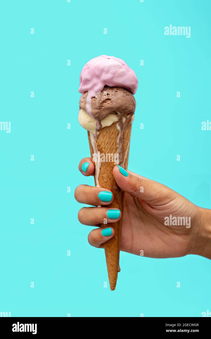Die Hand einer Frau hält einen Eiskegel, der auf einem hellblauen Hintergrund schmilzt Stockfoto