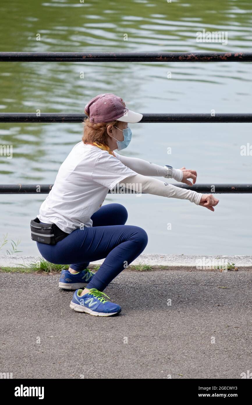 Eine flinke Frau in den Sechzigern macht vor dem Joggen tiefe Kniebeugeübungen. In einem Park in Queens, New York City. Stockfoto