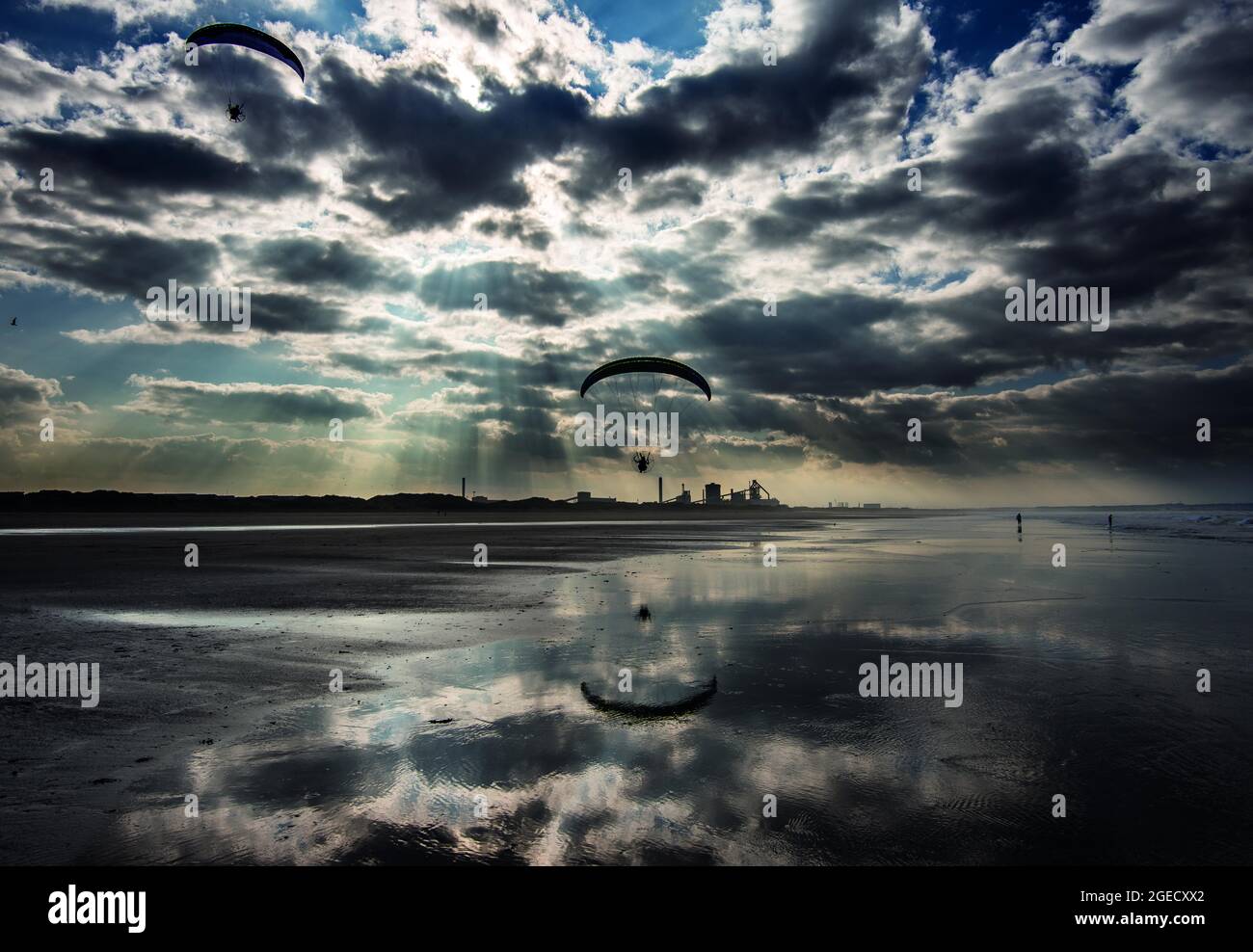 Gleitschirmfliegen über dem Strand von Coatham, mit dem ehemaligen Stahlwerk in der Ferne. Redcar, Cleveland, North Yorkshire, England Stockfoto