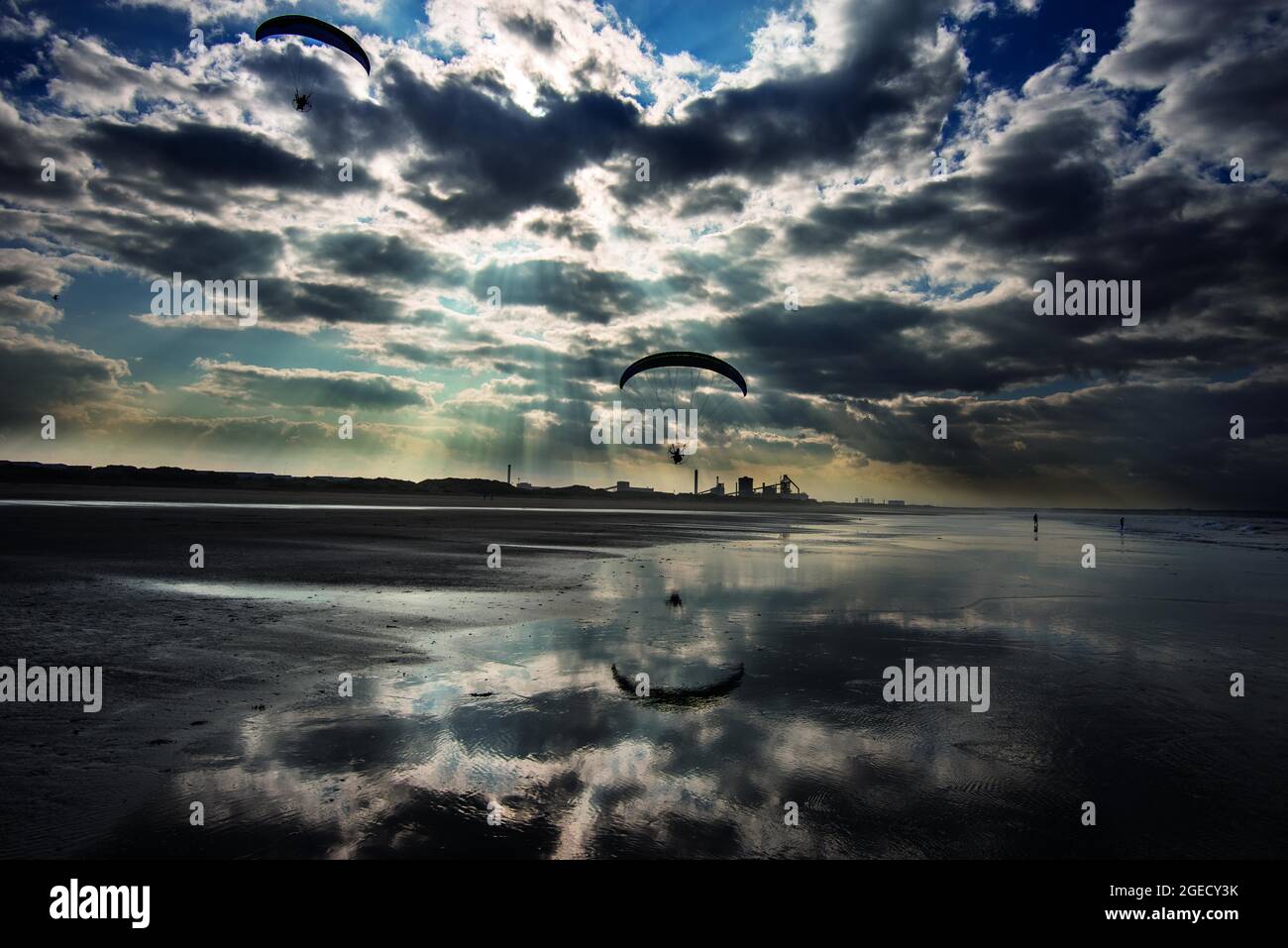 Gleitschirmfliegen über dem Strand von Coatham, mit dem ehemaligen Stahlwerk in der Ferne. Redcar, Cleveland, North Yorkshire, England Stockfoto