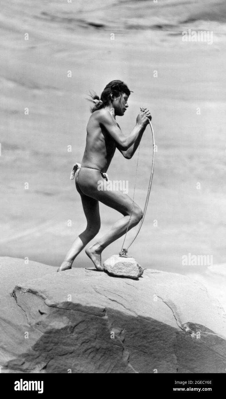 Roland Reed - Stringing the Bow - Ein Navajo-Mann, der auf einem Felsvorsprung steht, schnüren seinen Bogen - 1913 Stockfoto