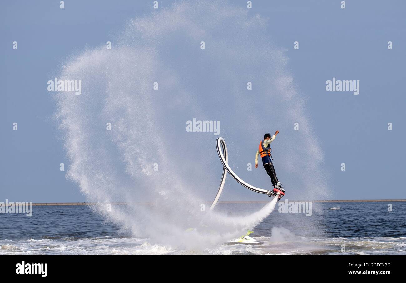 Ein Künstler führt eine Flying Trapeze-Show auf dem Meer durch. Stockfoto