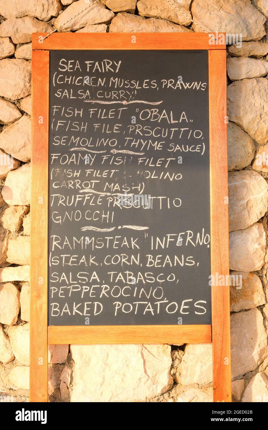 Schwarzes Tafelmenü, schwarze Farbe, Nachricht oder Werbung. Tafel steht in der Nähe des Restaurants an der Küste. Sonniger Tag. Stockfoto