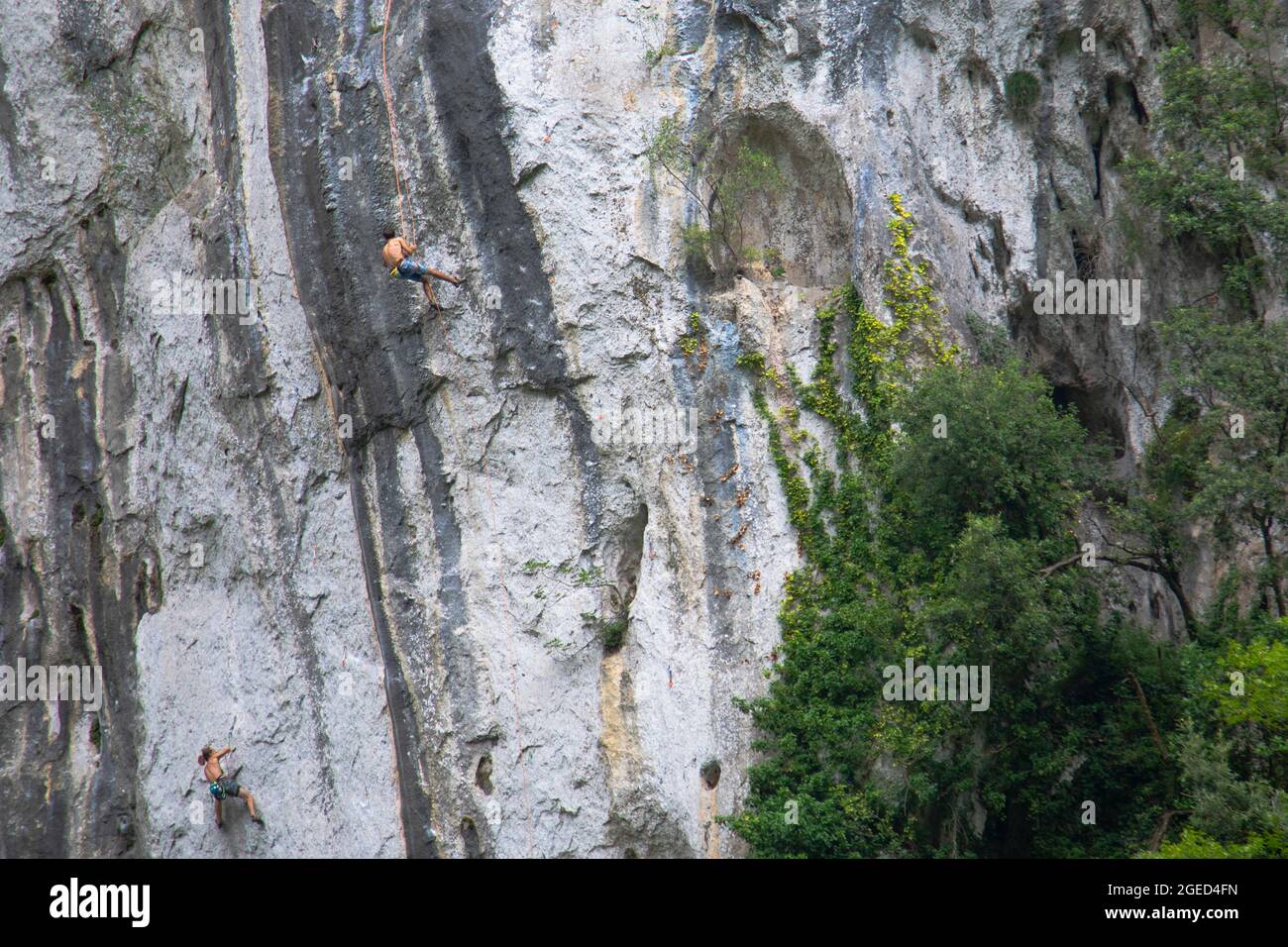 Blick aus der Ferne auf eine steile Klippe in den italienischen Alpen, kleine Figuren von Kletterern, die sie besteigen Stockfoto