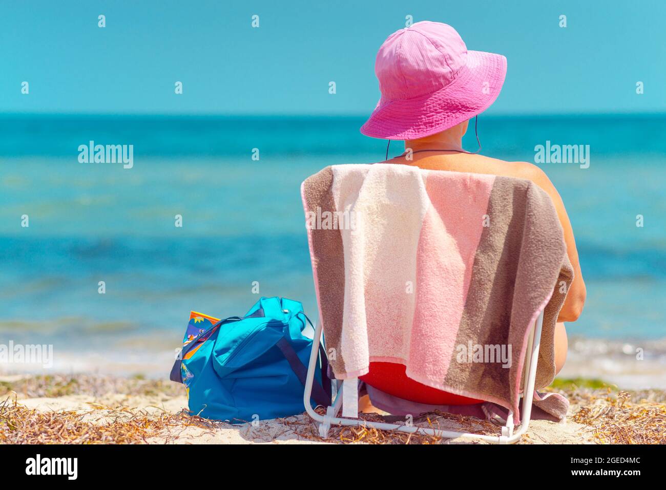 Körperpositive ältere Frau, die auf einem Stuhl am Strand sitzt Stockfoto
