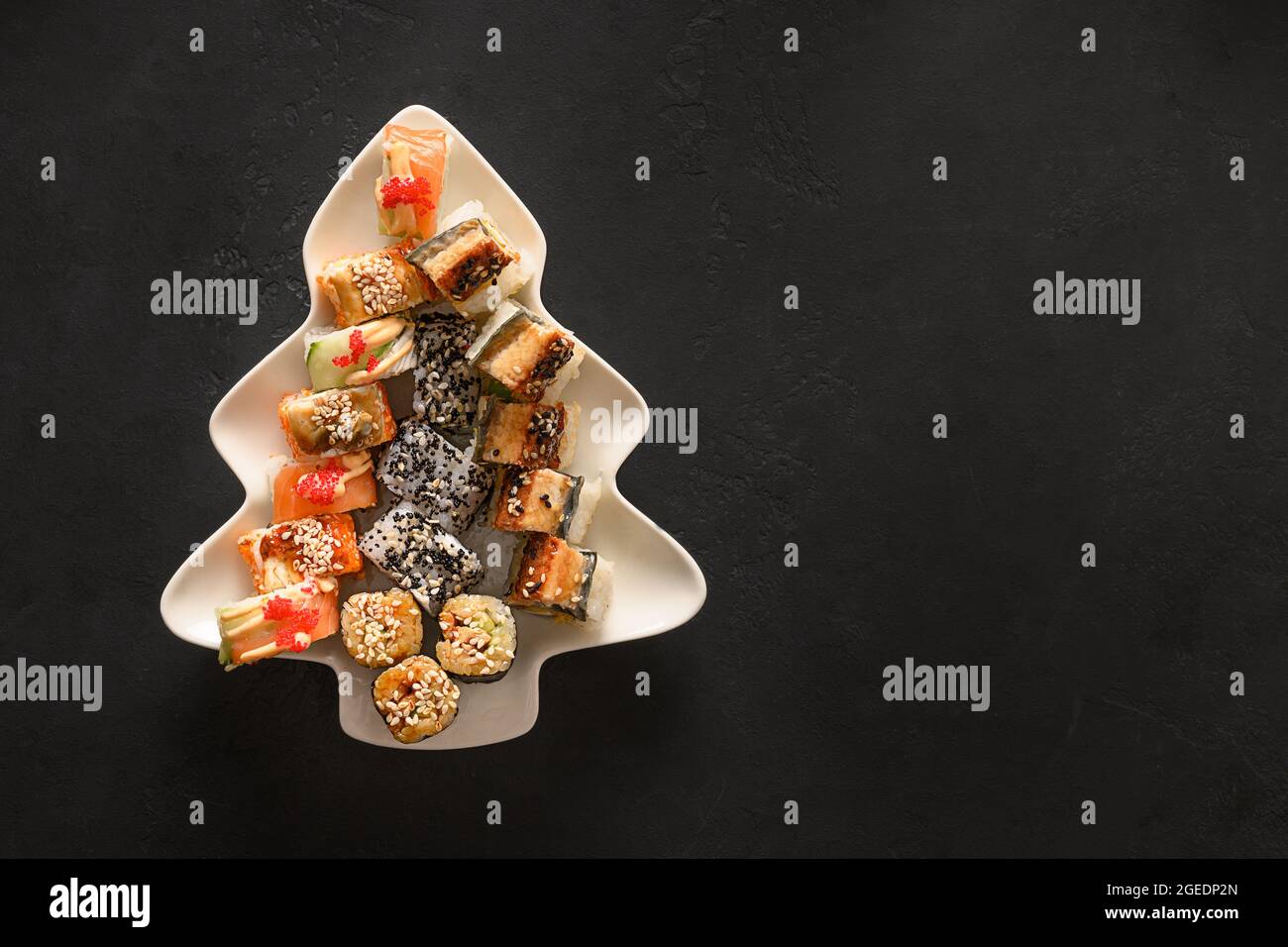 Sushi-Set serviert in einem blechförmigen Weihnachtsbaum auf schwarzem Hintergrund mit Platz zum Kopieren. Blick von oben. Stockfoto