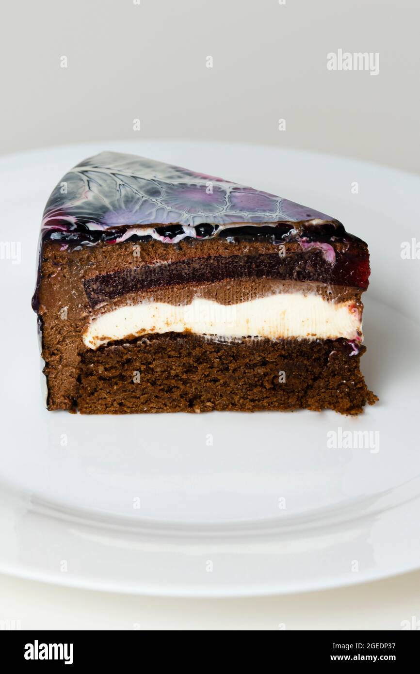 Nahaufnahme Mousse Cake bedeckt schwarz, rot und weiß Spiegelglasur. Französisches Dessert. Gefrorener Spiegel als Sahnehäubchen auf dem Kuchen. Backen und Süßwaren Konzept. Stockfoto