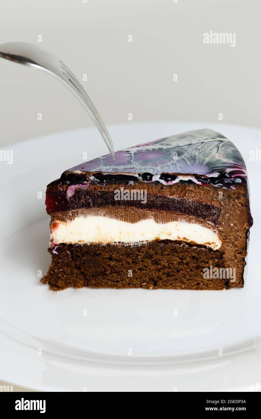 Nahaufnahme Mousse Cake bedeckt schwarz, rot und weiß Spiegelglasur. Französisches Dessert. Gefrorener Spiegel als Sahnehäubchen auf dem Kuchen. Backen und Süßwaren Konzept. Stockfoto