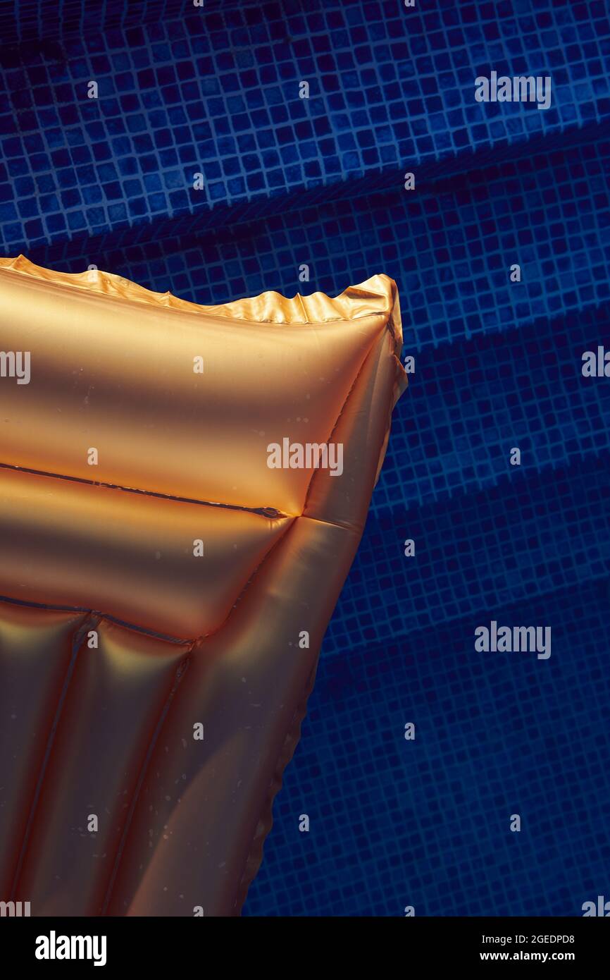 Goldene Schwimmmatratze im Pool gegen blaues Wasser bei Sonnenuntergang. Urlaub und Urlaub Konzept Foto. Freier Speicherplatz. Nahaufnahme von oben. Vertikal. Stockfoto