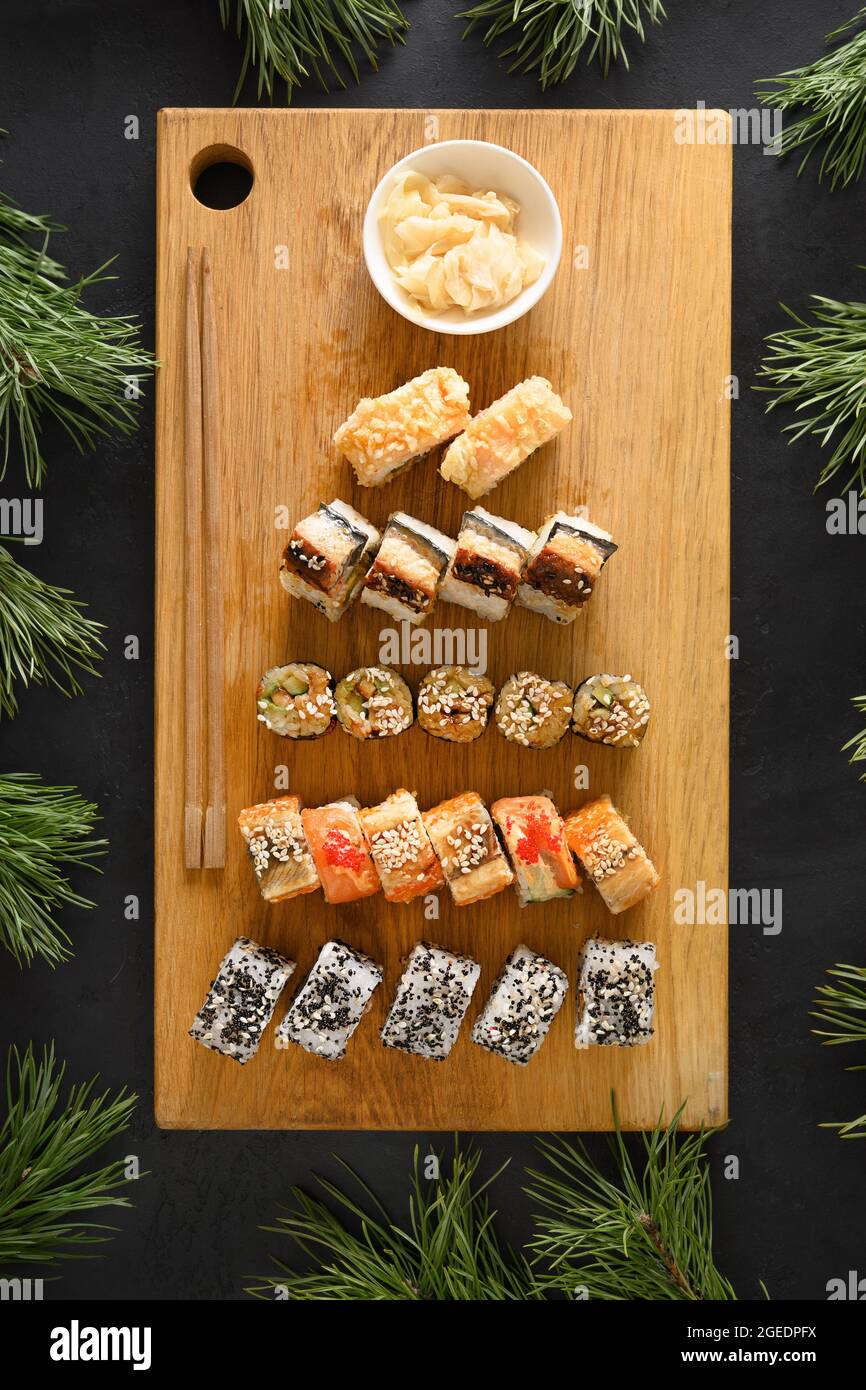 Sushi-Set serviert als Weihnachtsbaum auf Holzschneidebrett auf schwarzem Hintergrund. Blick von oben. Vertikales Format. Stockfoto
