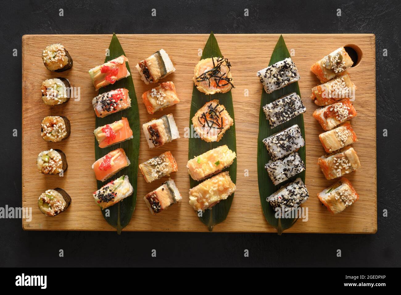 Sushi-Set auf Holzschneidebrett auf schwarzem Hintergrund. Blick von oben. Flach liegend. Stockfoto