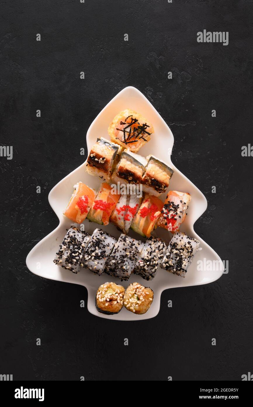 Sushi-Set serviert in Teller als Weihnachtsbaum mit festlicher Dekoration auf schwarzem Hintergrund. Blick von oben. Stockfoto