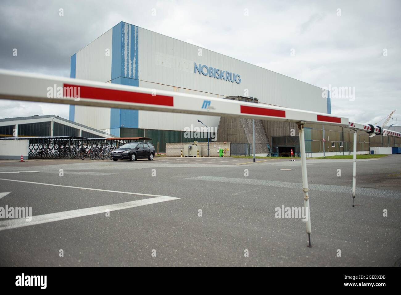 Rendsburg, Deutschland. August 2021. Hinter einer Schranke am Fabriktor der Nobiskrug-Werft ist eine Fabrikhalle zu sehen. Die Werft am Nord-Ostsee-Kanal in Rendsburg wurde von der Flensburger Schiffbau-Gesellschaft übernommen. Quelle: Gregor Fischer/dpa/Alamy Live News Stockfoto
