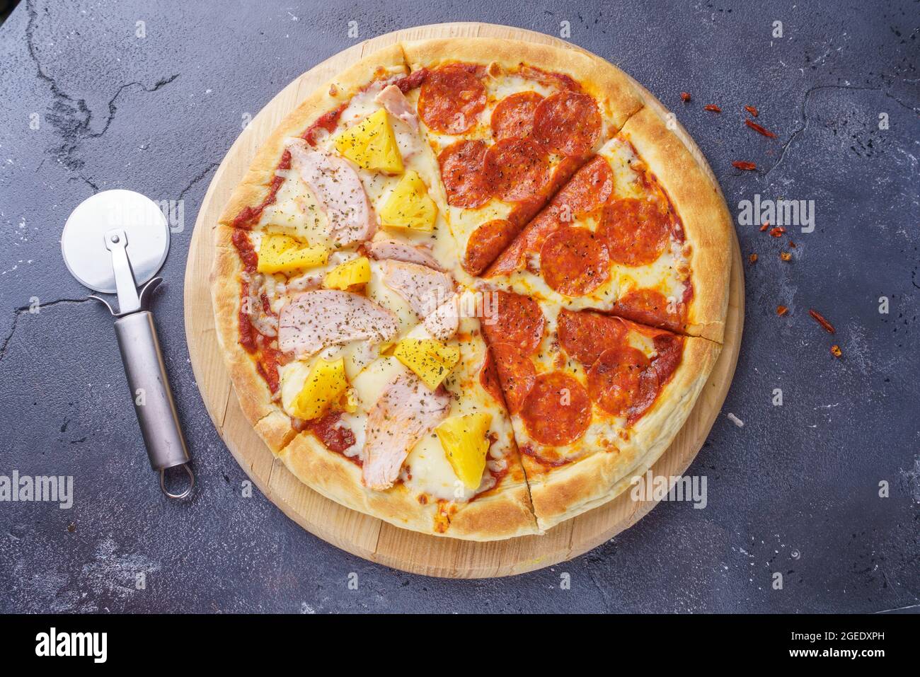 Pepperoni Pizza und Ananas Pizza auf dem gleichen Brett mit einem runden Pizzamesser Stockfoto