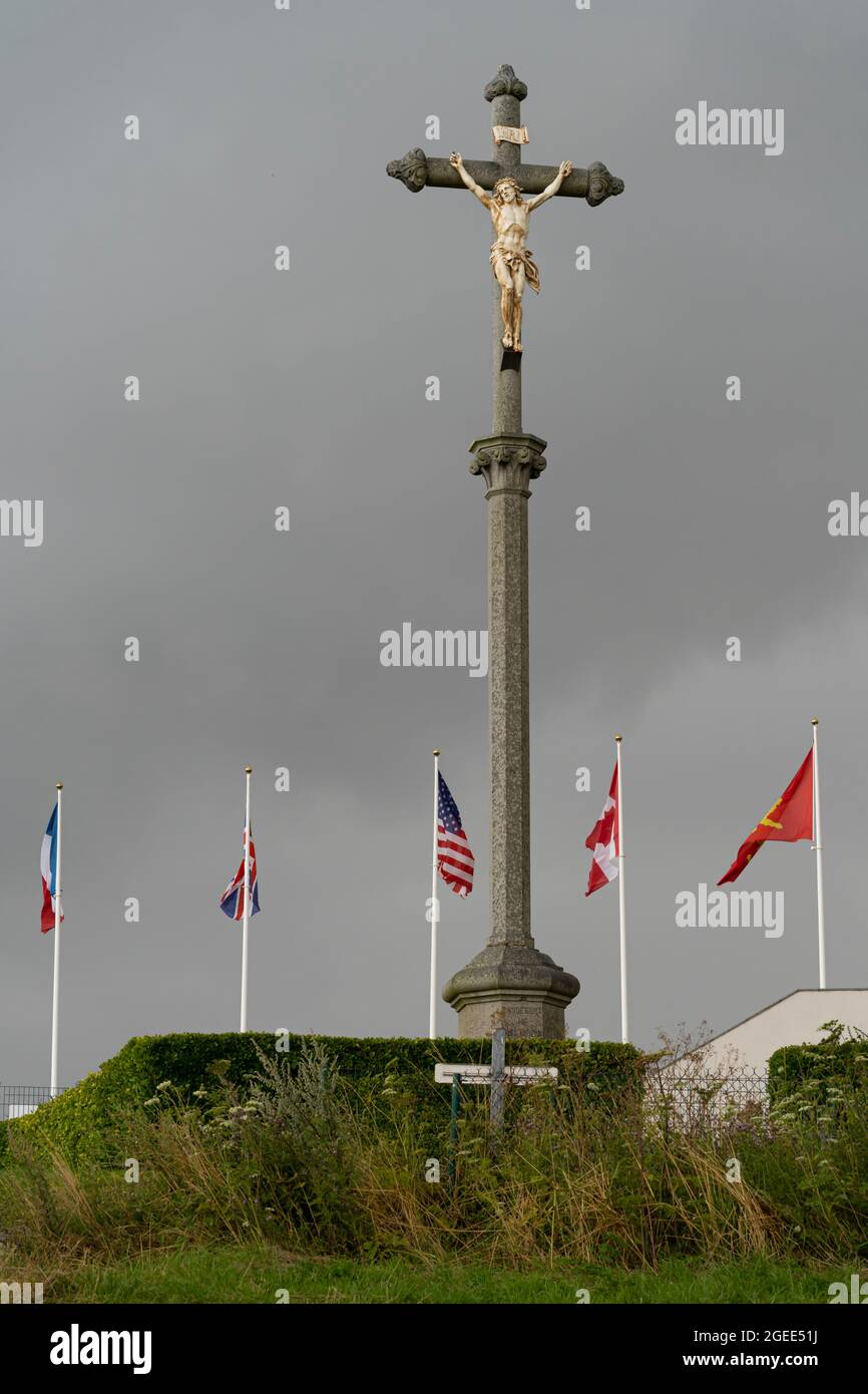 Arromanches-les-Bains, Frankreich - 08 03 2021: Der Kalvarienberg und die Flaggen der Alliierten des Zweiten Weltkriegs in einem regnerischen Himmel Stockfoto