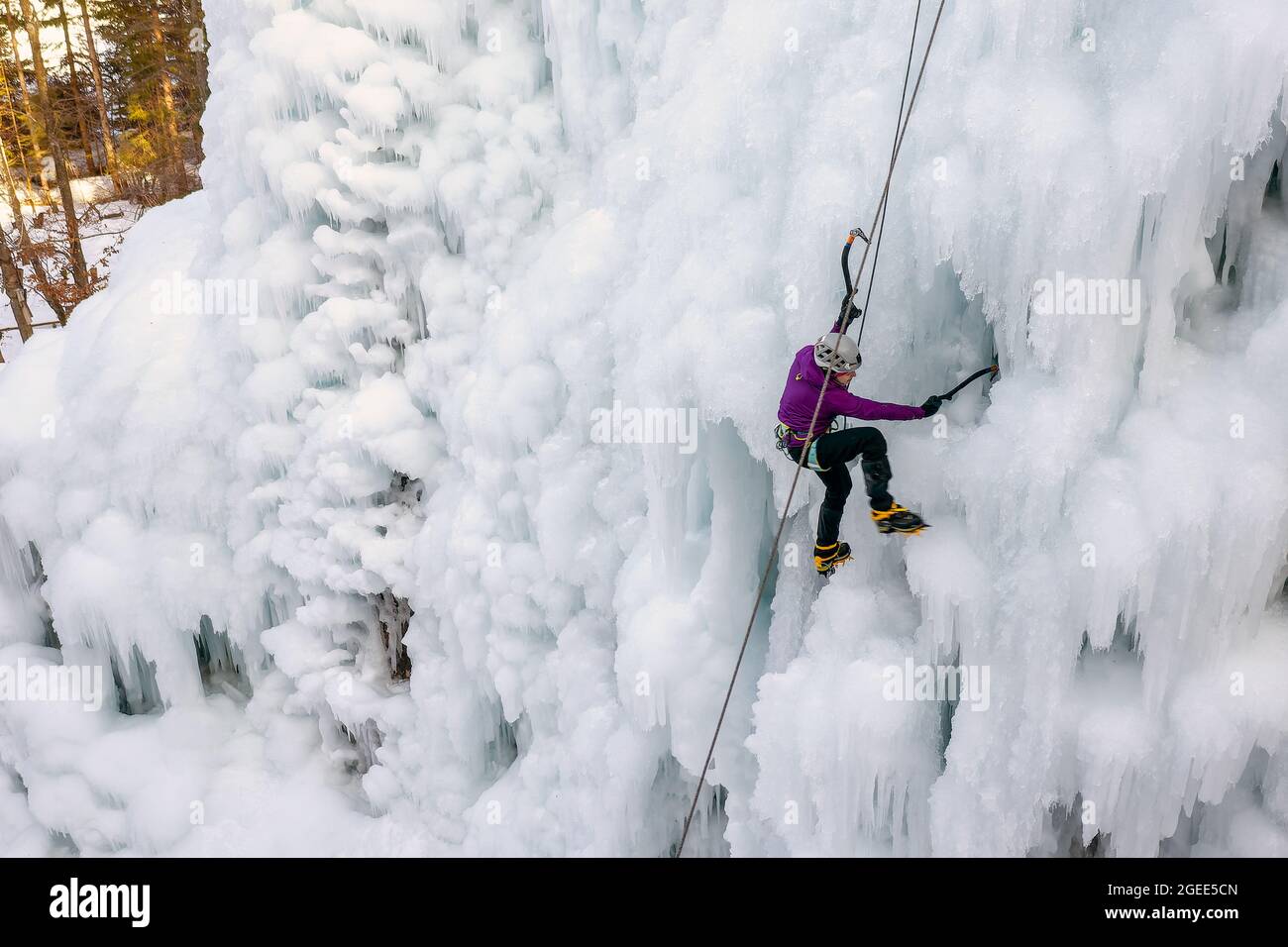 Alpinistin mit Eiskletterausrüstung, Axt und Kletterseilen, Klettern an einem gefrorenen Wasserfall, Blick von unten Stockfoto