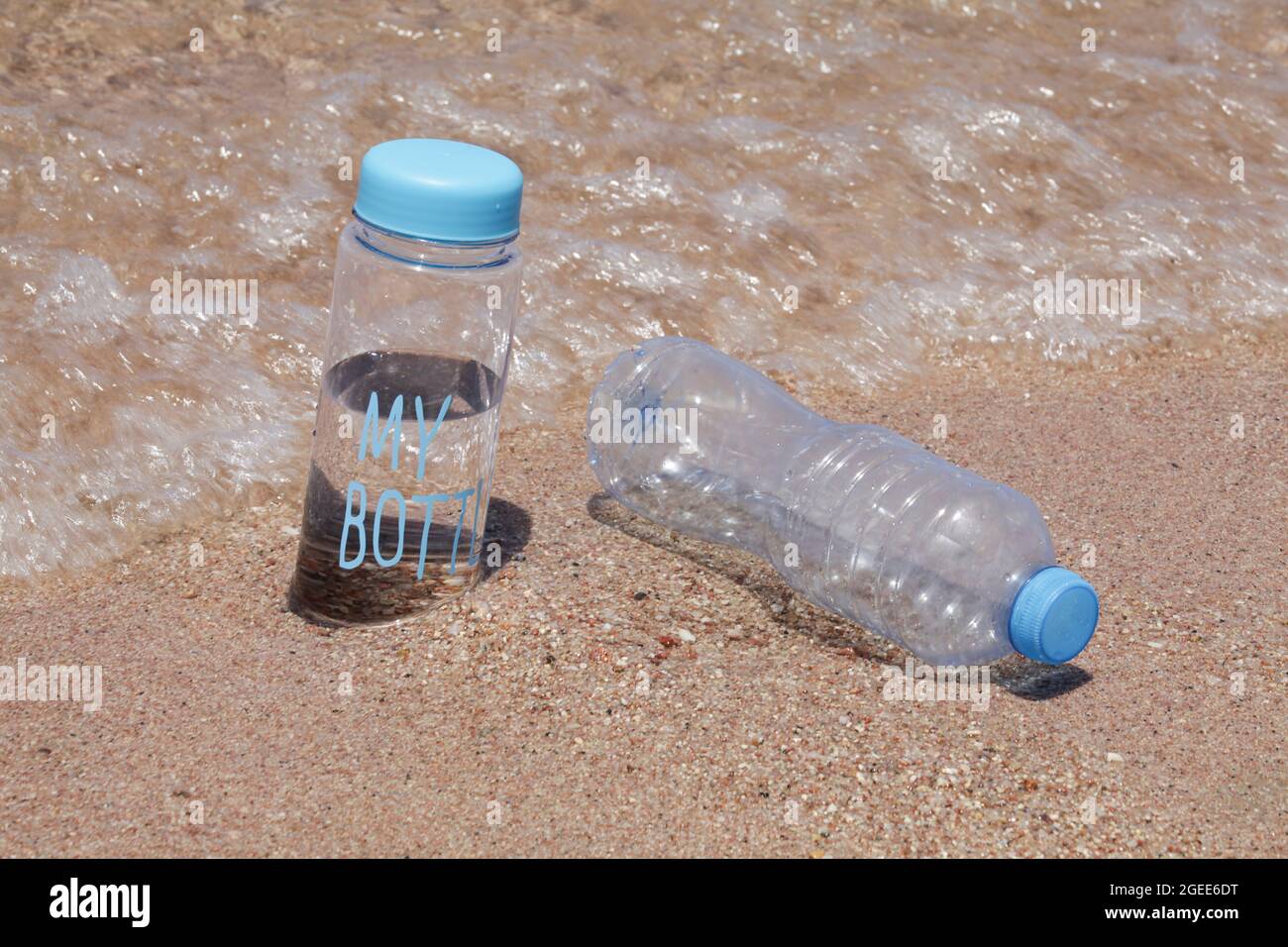 Wiederverwendbare Wasserflasche gegen Plastikflasche am Strand in der Nähe des Meeres. Reduzieren Sie das Plastik, Null Abfall Konzept. Stockfoto