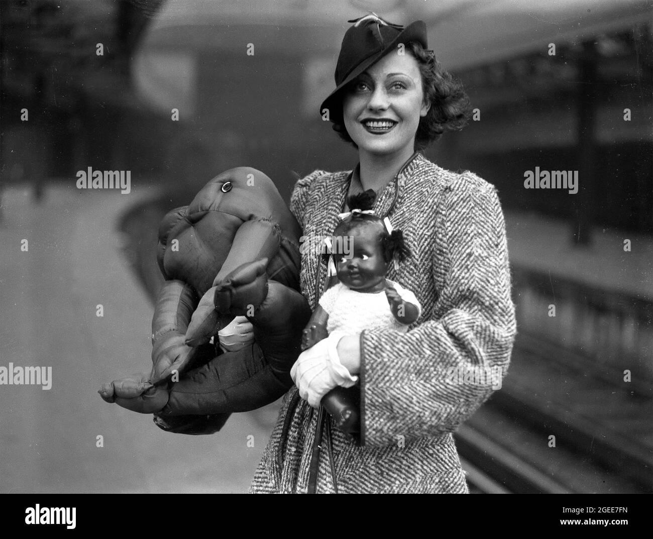 Hübsche Frau mit einer schwarzen Topsy-Puppe und einem weichen Spielzeug-Frosch in Victoria Station, London, 1930 Stockfoto