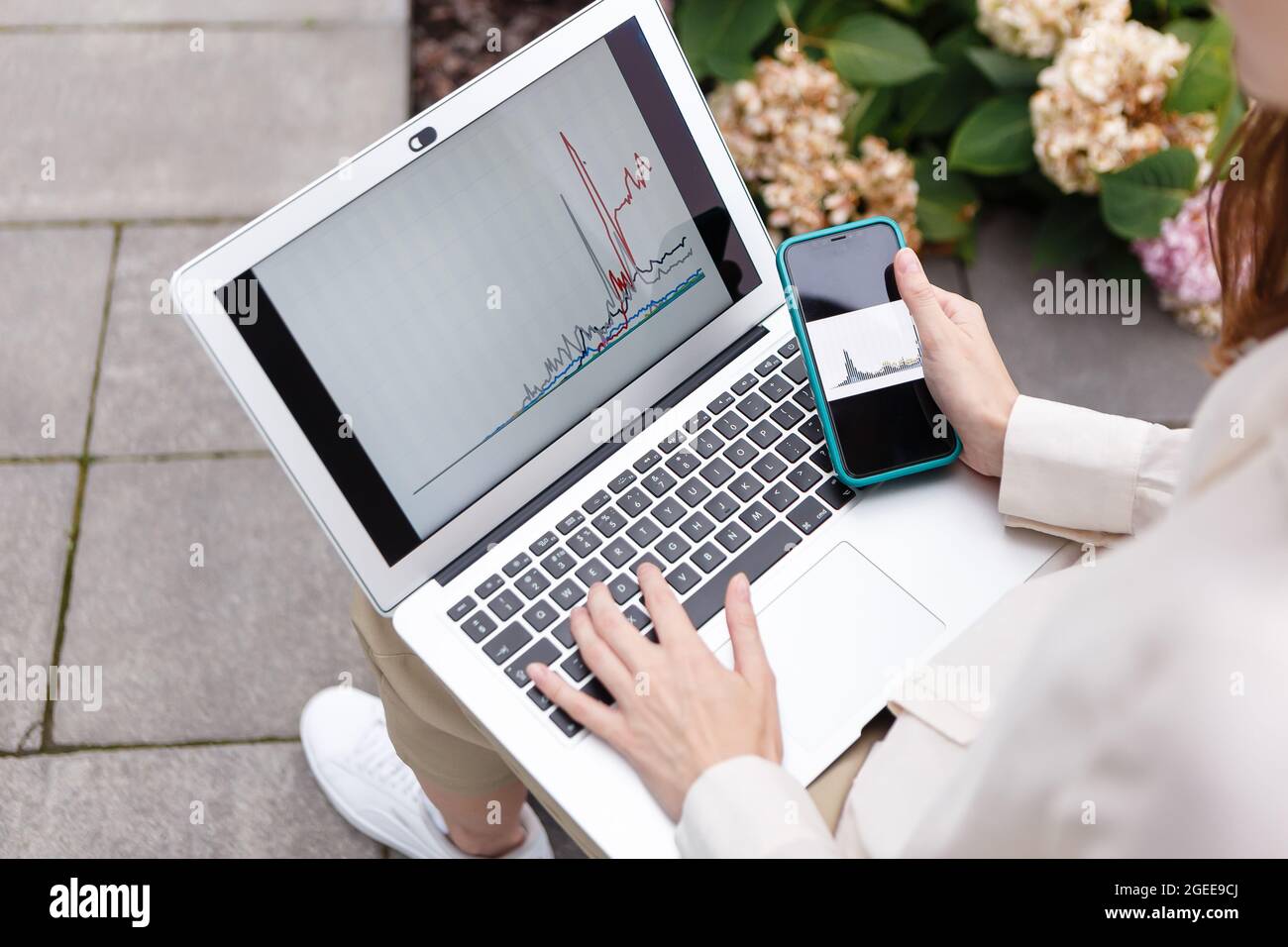 Frau mit Laptop und Smartphone, die Bitcoin-Wachstumsdiagramm beobachtet Stockfoto