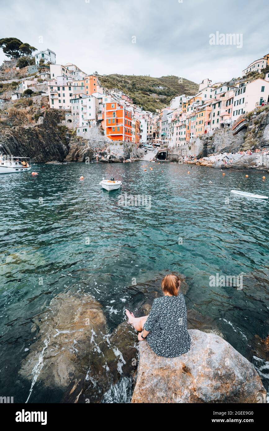 Junge Frau, die auf einem Felsen sitzt und die Bucht des berühmten italienischen Dorfes überblickt Stockfoto