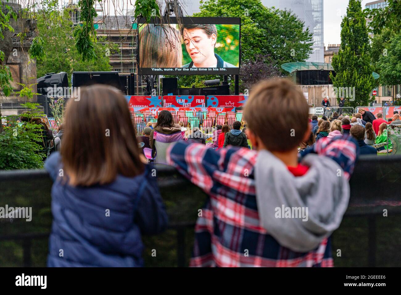 Edinburgh, Schottland, Großbritannien. August 2021. Das Publikum sieht sich eine Vorführung des Kultfilms Ferris Bueller’s Day Off auf dem Film Fest im Freiluftkino der Stadt auf dem St. Andrew Square im Freien an. Dies ist eine der Veranstaltungen, die während des Edinburgh International Film Festival in der Stadt stattfinden. PIC; Junge Filmbesucher beobachten die Vorführung von über dem Zaun. Iain Masterton/Alamy Live Nachrichten. Stockfoto