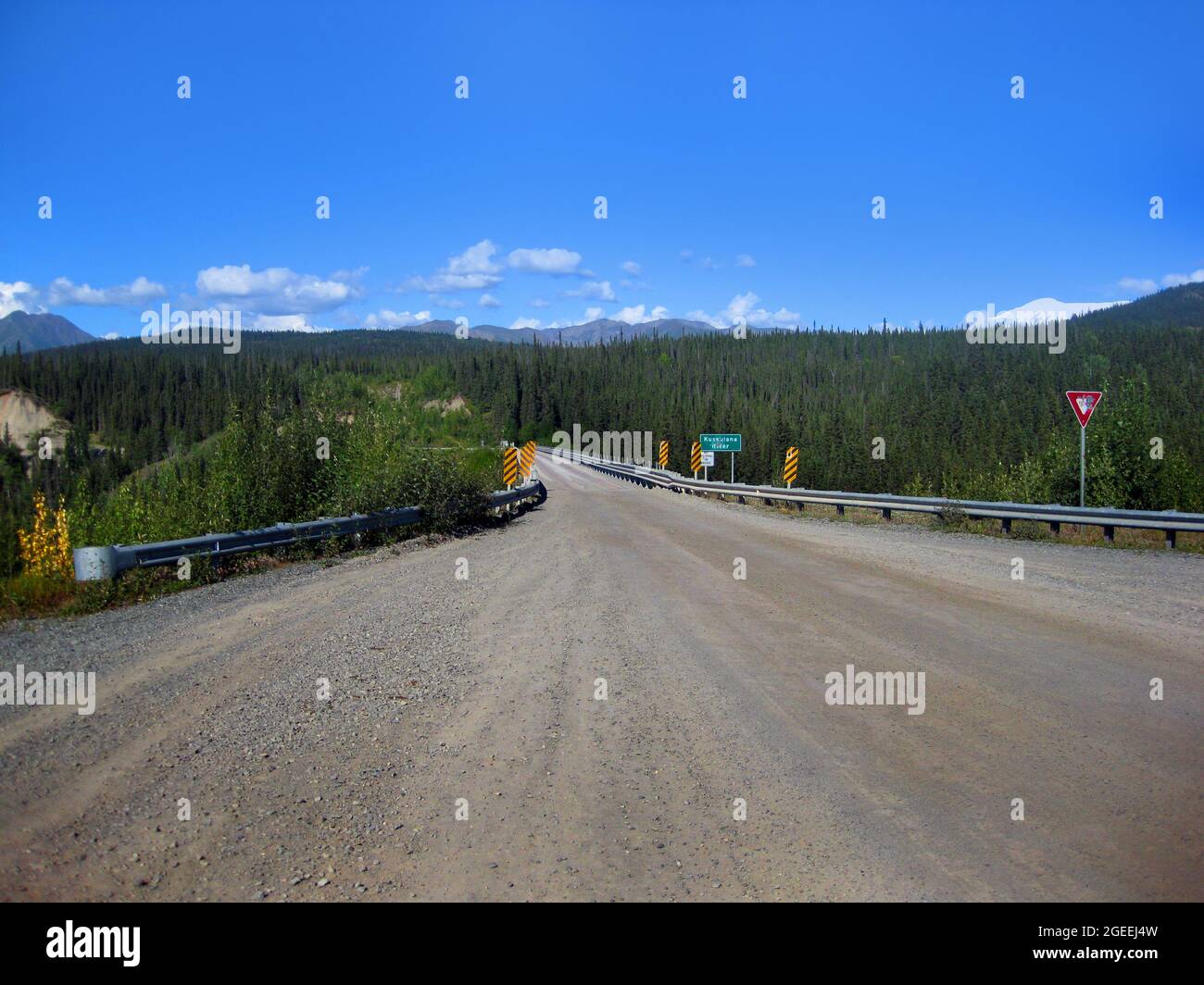 Schotterstraße nähert sich der Kuskulana River Bridge auf dem Alaskan Highway. Bergketten liegen in der Ferne und grüner Wald bedeckt näher gelegenen Bergen Stockfoto
