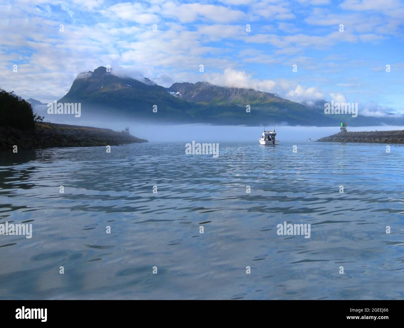 Fischerboot manuevers to open waters on the Bay of Valdez, Alaska. Am frühen Morgen steigt Nebel und Nebel aus dem Wasser auf und liegt über den Bergen. Stockfoto