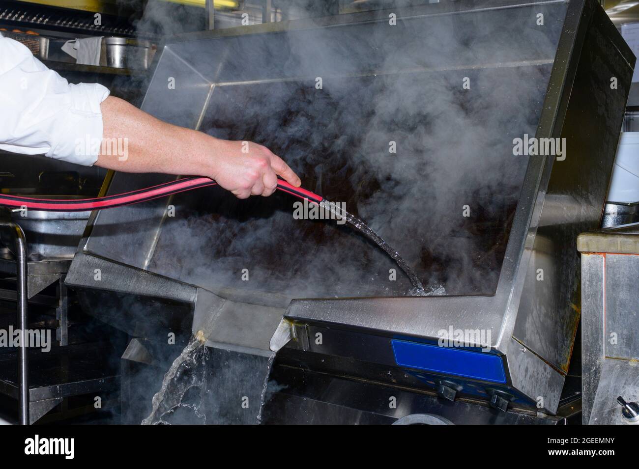 Ein Koch reinigt die große elektrische Pfanne mit Schlauch und Wasser Stockfoto