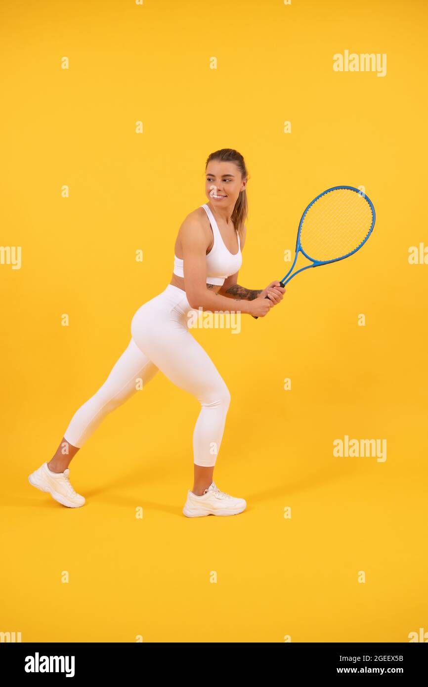 Lächelnder Tennisspieler läuft mit Schläger auf gelbem Hintergrund, Sport Stockfoto