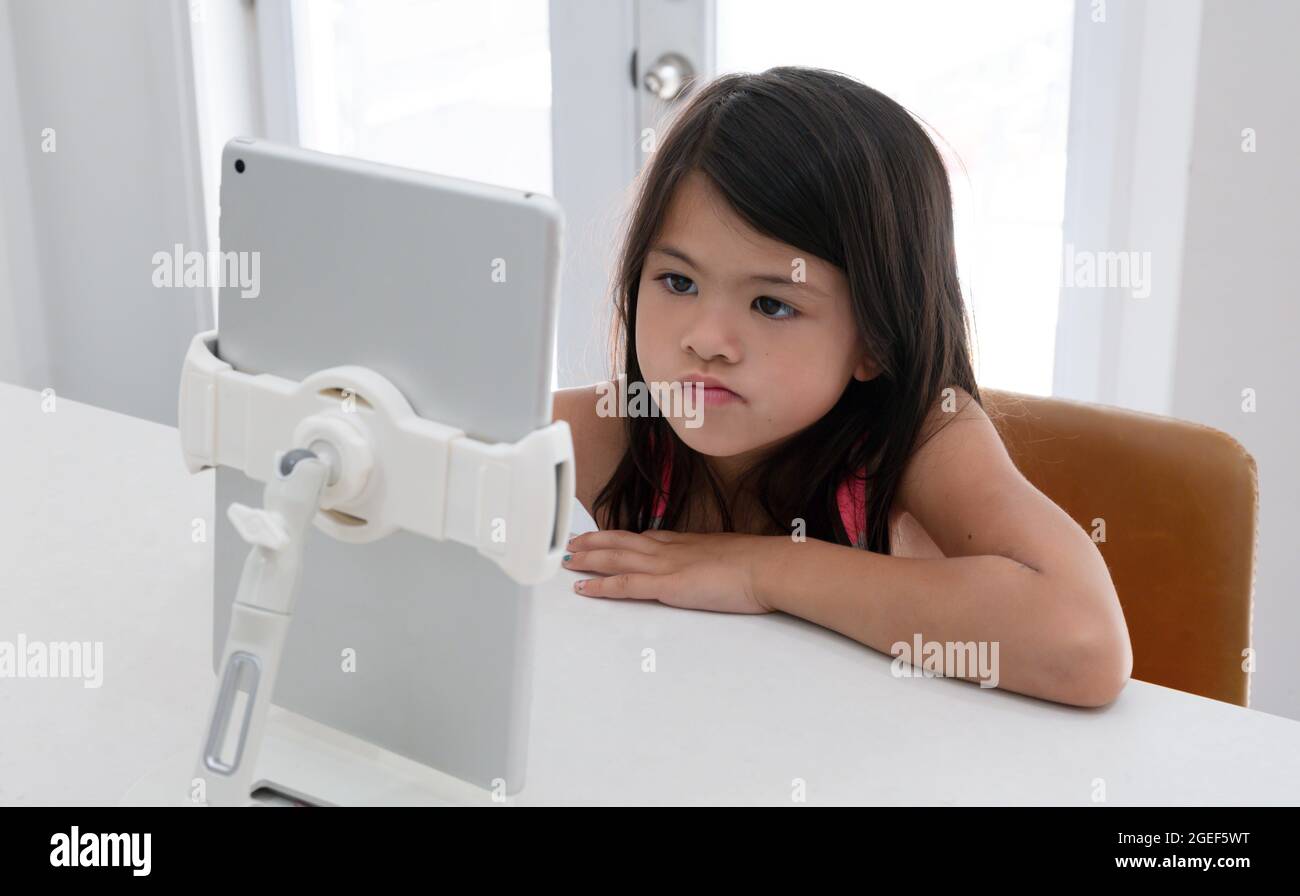 Biracial Mädchen mit einem kontemplativen Ausdruck homeschooling am Küchentisch während covid Lockdown Stockfoto