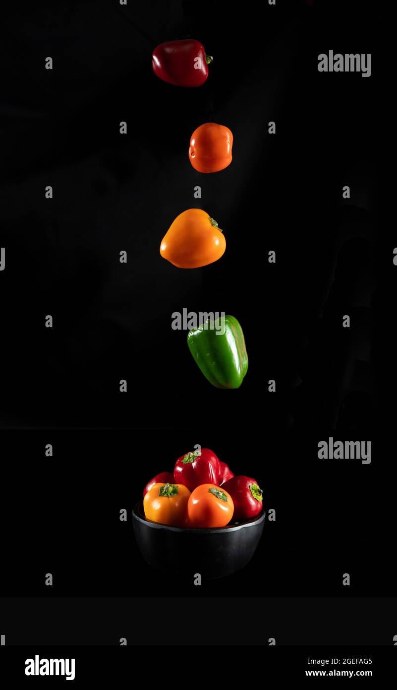 Vertikale Aufnahme von bunten Paprika in und über einer Schüssel, vor einem schwarzen Hintergrund Stockfoto