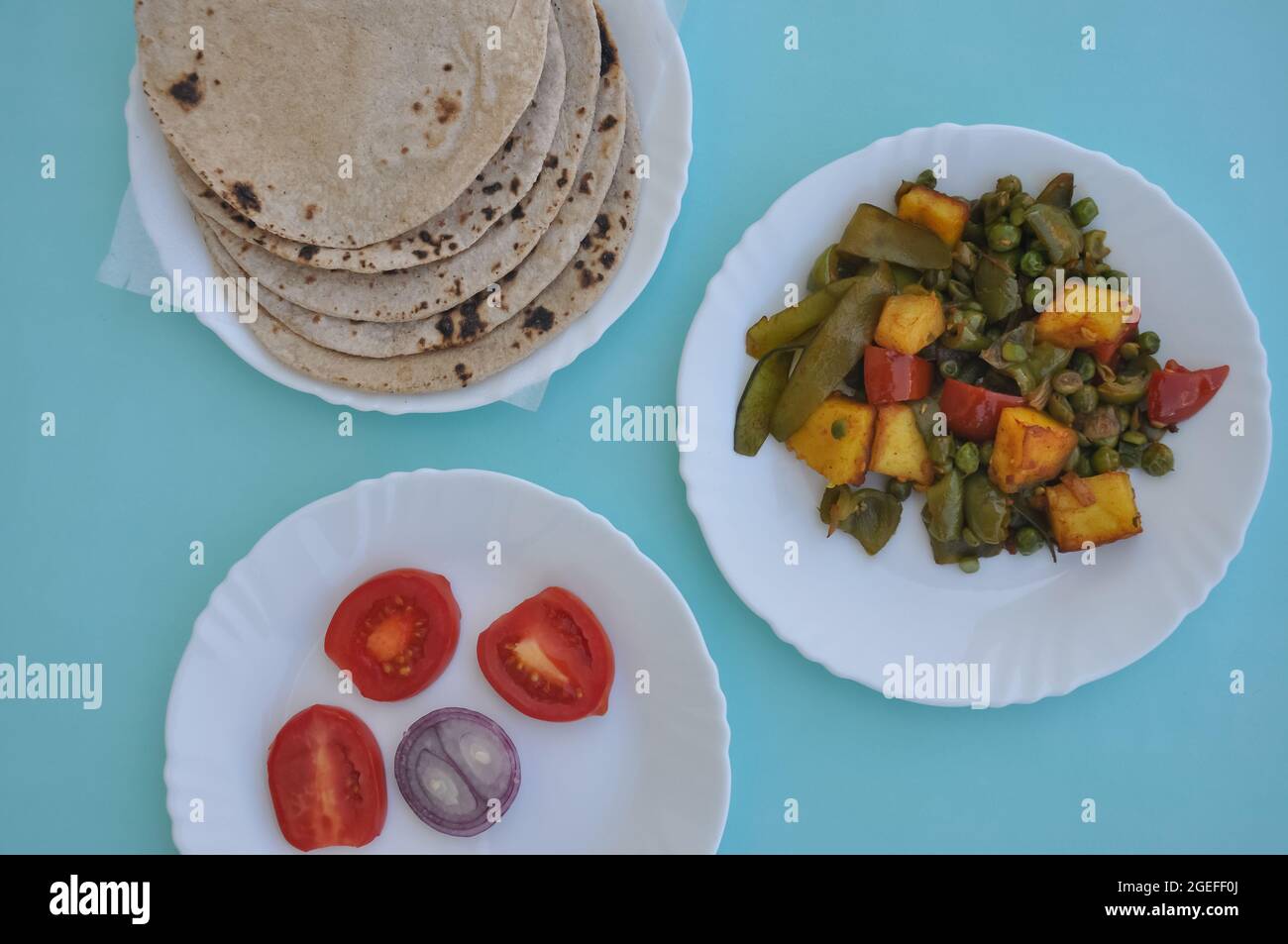 Indian Food - Matar Paneer Gemüse, Roti und Salat auf weißem Teller mit hellblauem Hintergrund Stockfoto
