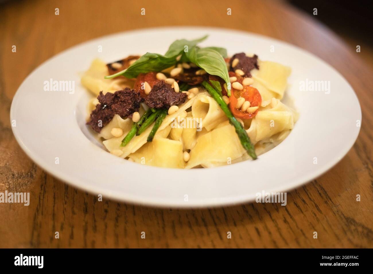 Jerusalem Artischockencreme pappardelle: Ein veganes Gericht mit Pasta, gerösteten Kirschtomaten, Olivenaufstrich, Spargel, Pinienkernen und Basilikum auf einem Teller Stockfoto