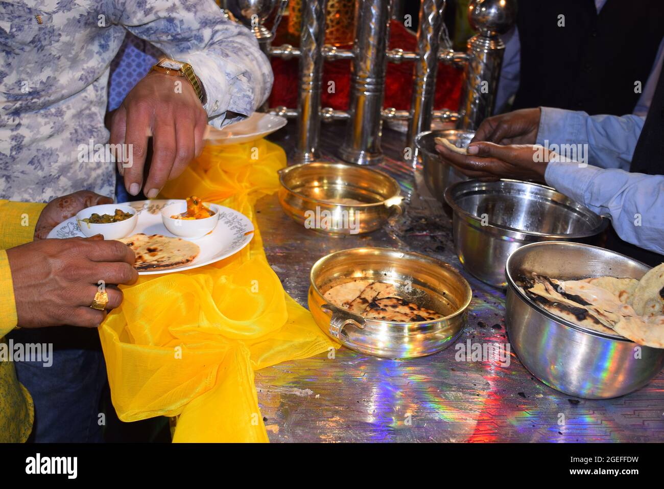 Hand eines indischen Mannes, der Tandoori Roti aus einem großen Topf in seinem Teller trug Stockfoto