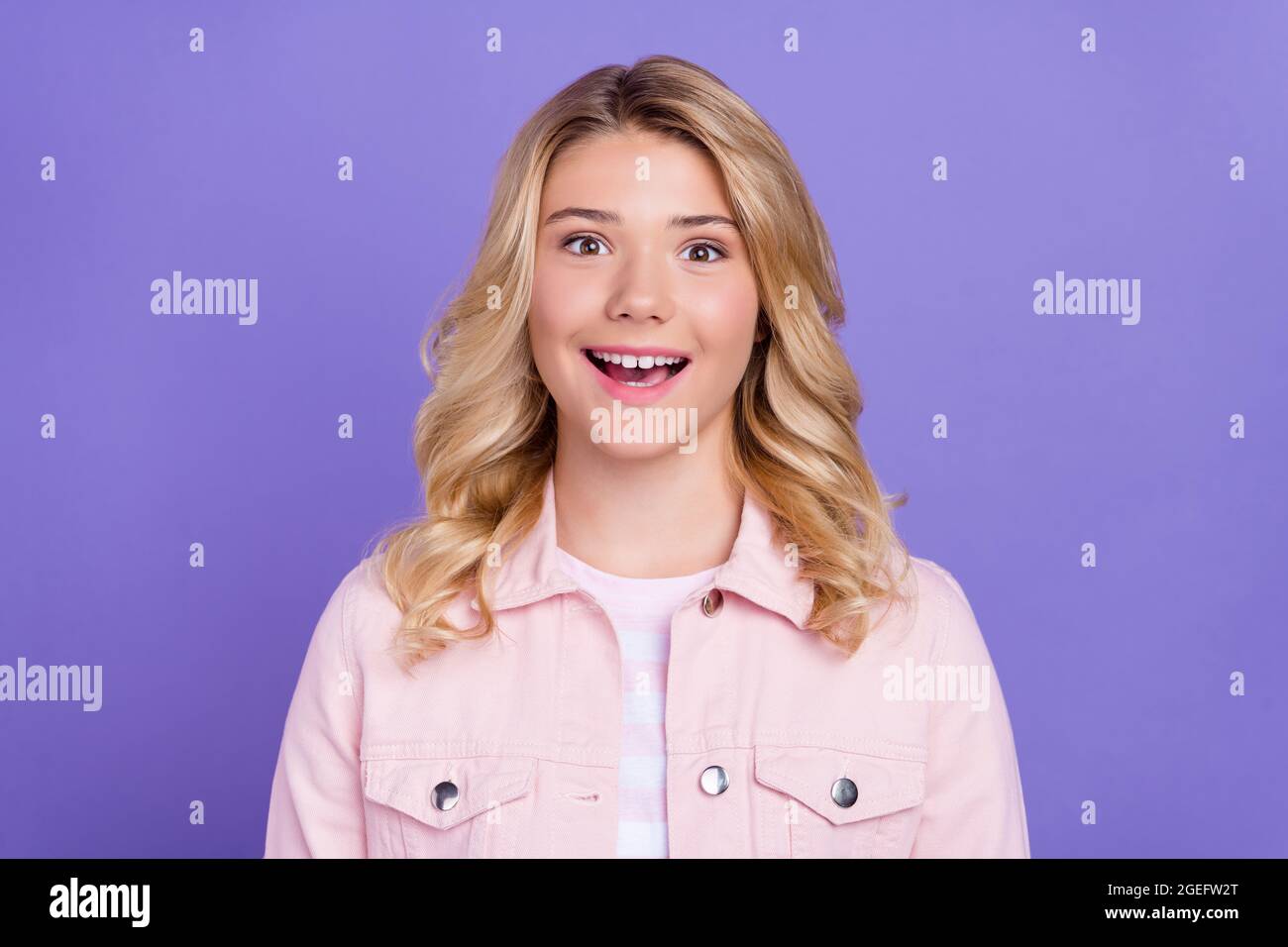 Foto von beeindruckt charmante Schulmädchen gekleidet rosa Kleidung offenen Mund lächelnd isoliert lila Farbe Hintergrund Stockfoto