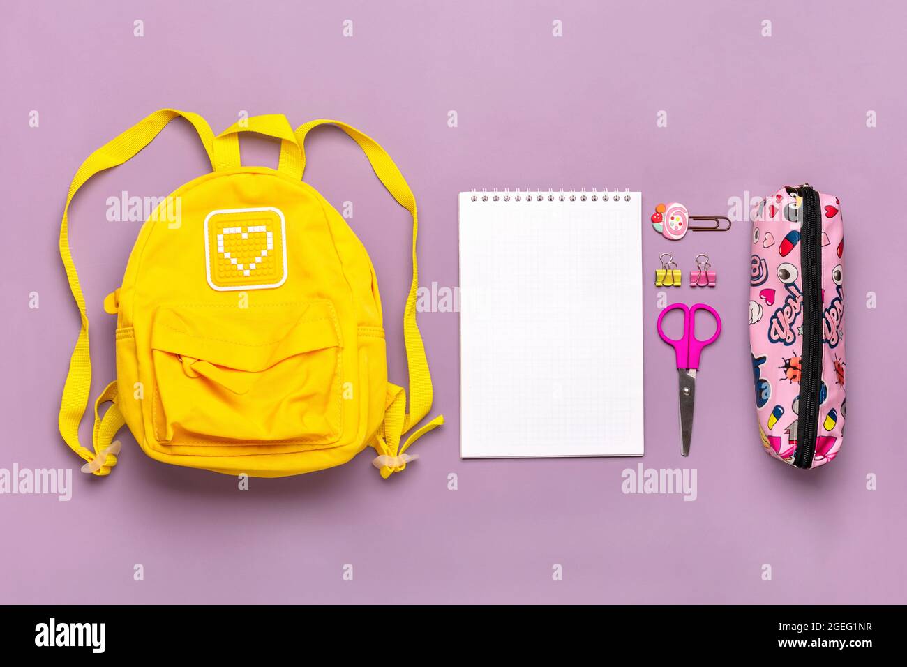Zurück zur Schule, Bildungskonzept. Gelber Rucksack mit Schulbedarf - Notizbuch, Stifte, Clips, Schere isoliert auf violettem Hintergrund Draufsicht Copy Stockfoto