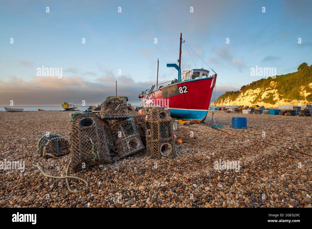 Hummertöpfe und rotes Fischerboot am Kiesstrand bei Sonnenaufgang, Bier, Jurassic Coast, Devon, England, Vereinigtes Königreich, Europa Stockfoto