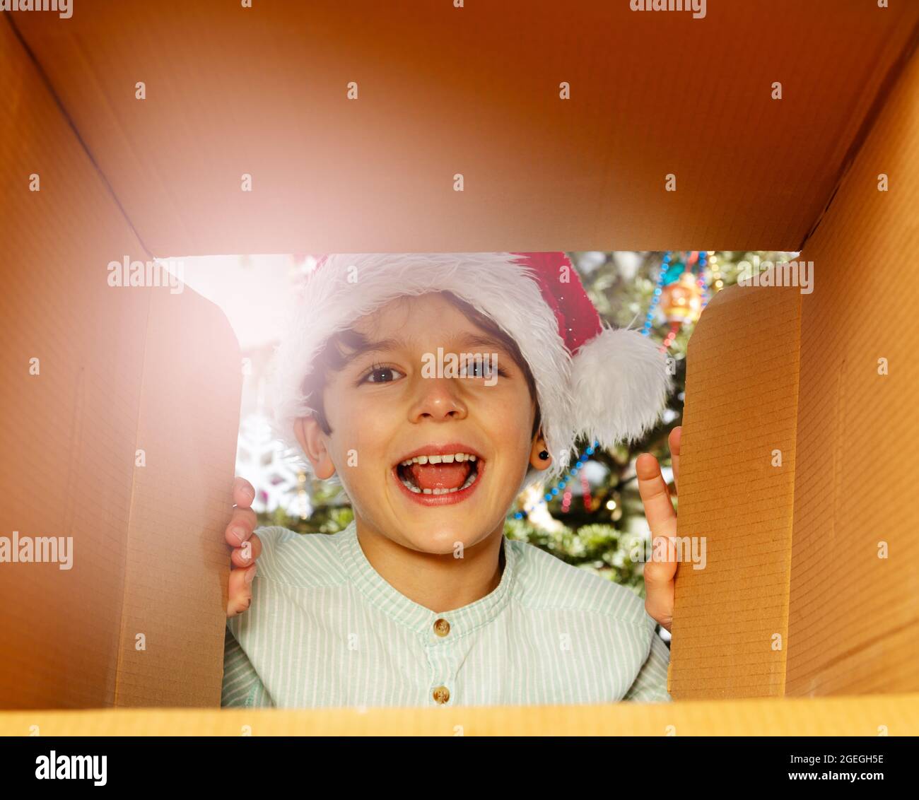 Lachender Junge im Weihnachtsmütze schaut in die Geschenk-Box Stockfoto