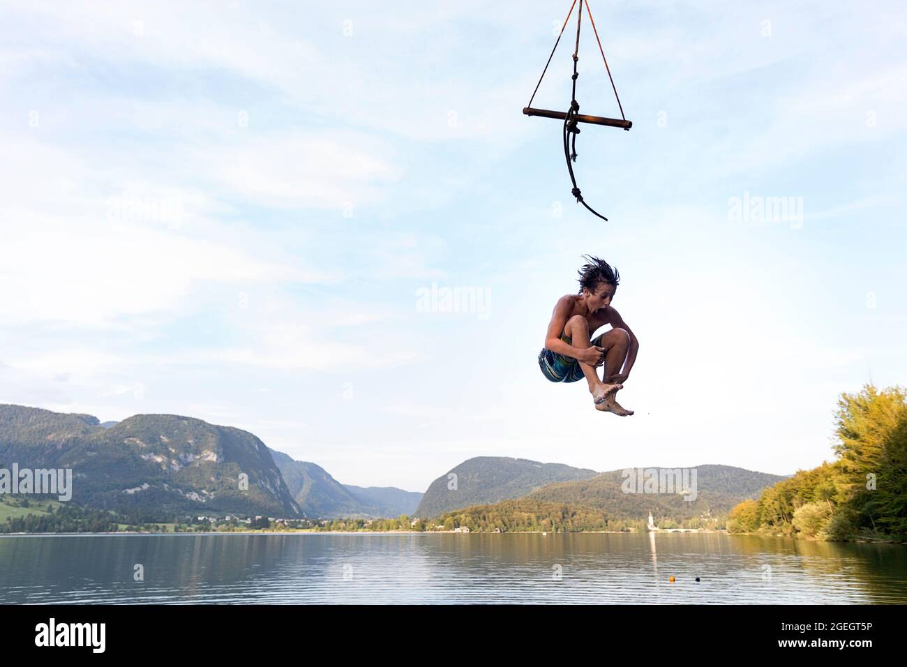 Ein Junge, der an einem wunderschönen Sommertag auf dem Bohinjsee in Slowenien von einer Baumschaukel springt Stockfoto