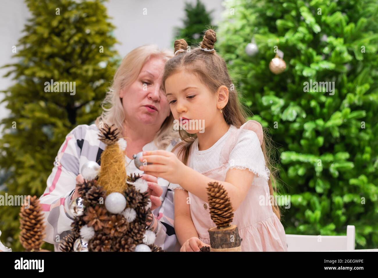 Ältere kaukasische Frau, die mit zwei Enkelinnen Tannenzapfen zu weihnachten schmückende Stockfoto