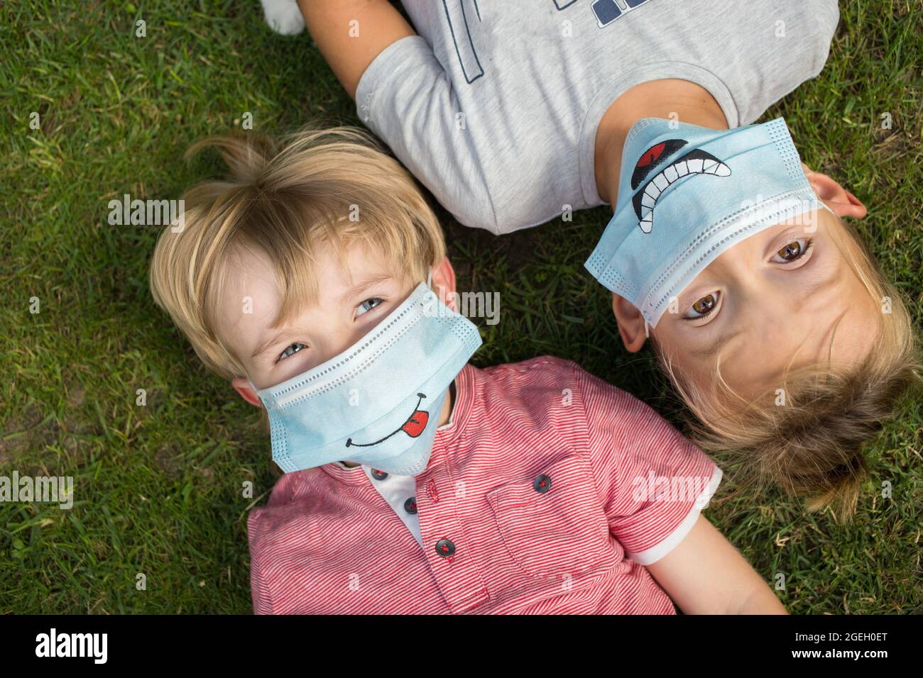 Porträt von zwei Jungen 5-6 Jahre alt in medizinischen Schutzmasken mit lustigen Lächeln gezeichnet. Liegen auf dem Rücken auf dem Rasen, Blick nach oben. Kommunikation zwischen Kind Stockfoto