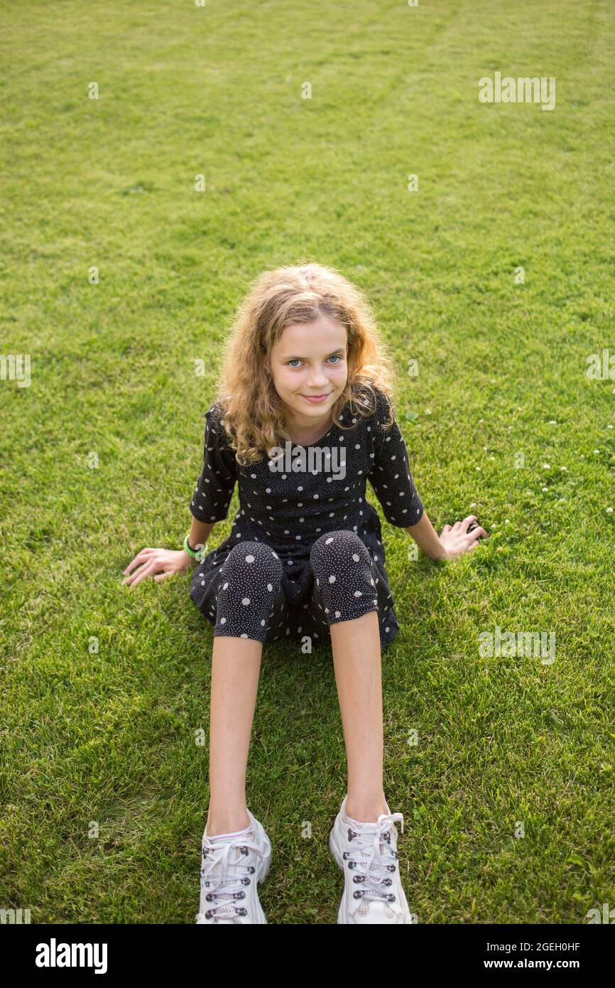 Portrait von lächelnden schönen Teenager-Mädchen 12 Jahre alt sitzt auf dem Rasen an einem sonnigen Tag. Genießen Sie die Natur an der frischen Luft, Entspannung, Träume. Joyf Stockfoto