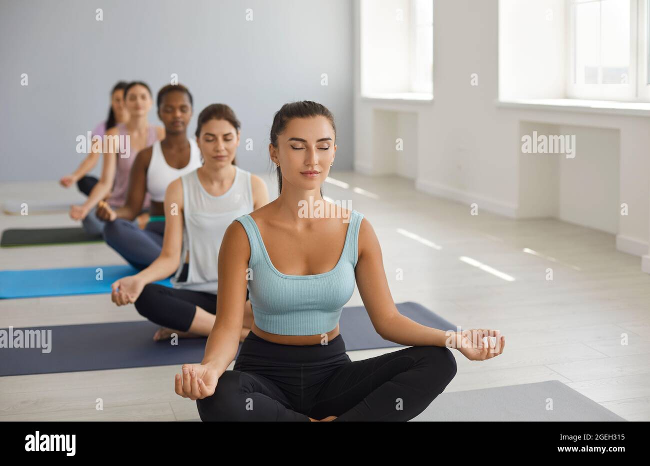 Eine Gruppe afroamerikanischer und kaukasischer Sportfrauen, die Yoga-Kurse praktizieren und in Suhasana Pose sitzen. Stockfoto