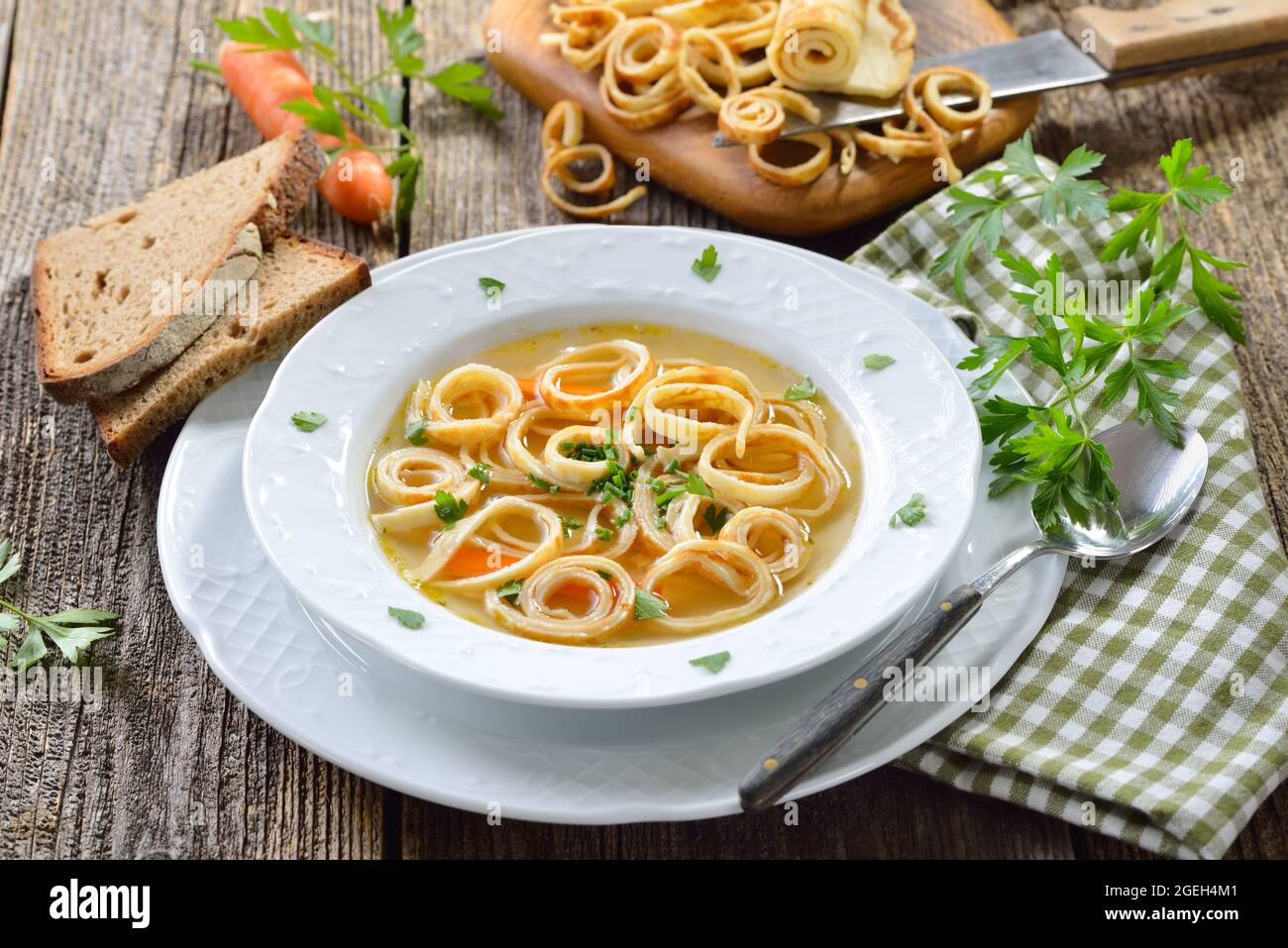 Köstliche hausgemachte Rinderbrühe mit Pfannkuchenstreifen, serviert mit Brot auf einem Holztisch Stockfoto