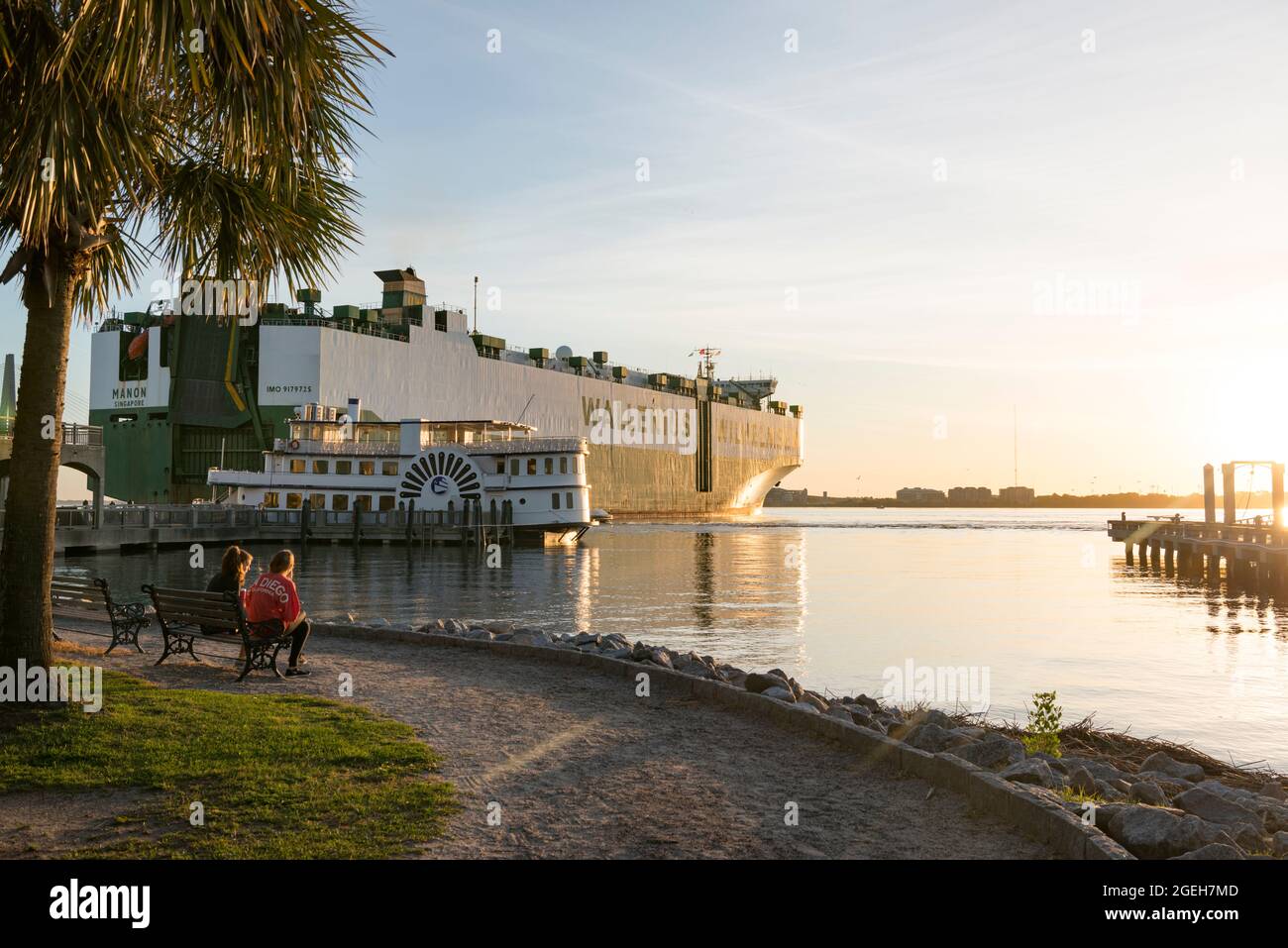 Ein riesiges Frachtschiff, das neben einem Raddampfer auf dem Cooper River in der Innenstadt von Charleston, South Carolina, USA, festmacht Stockfoto