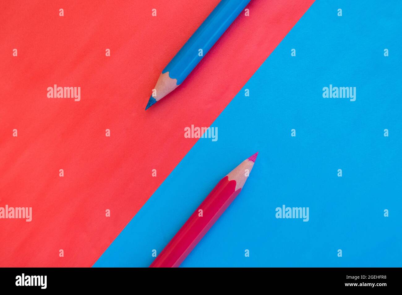 Rosa und blauer Hintergrund diagonal geteilt mit zwei passenden Farbstiften auf gegenüberliegenden Farben platziert. Draufsicht flach liegend mit Platz für Text Stockfoto