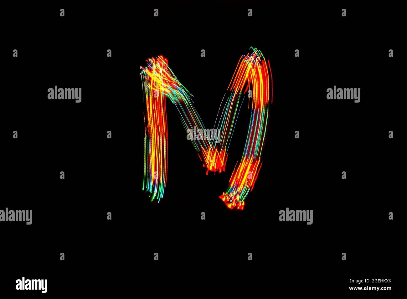 Buchstabe M. Leichte Malerei Alphabet. Langzeitbelichtung. Zeichnungsbuchstabe M mit bunten Lichtern auf schwarzem Hintergrund. Stockfoto