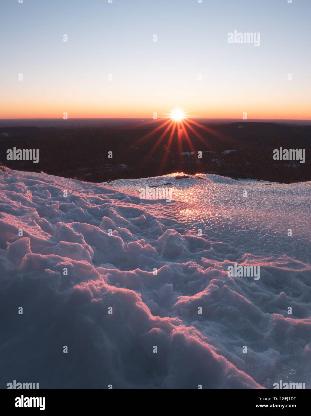 Sonnenaufgang vom Gipfel des Mount Watatic in Ashburnham Massachusetts an einem kalten, verschneiten Wintermorgen. Die aufgehende Sonne bildet einen Sonnenstern. Stockfoto