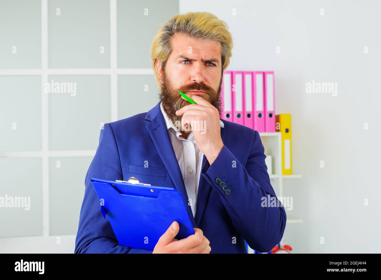 Selbstbewusster Geschäftsmann im Büro. Bärtig schöner Mann mit Notizblock. Nachdenkliche Führungskraft am Arbeitsplatz. Stockfoto