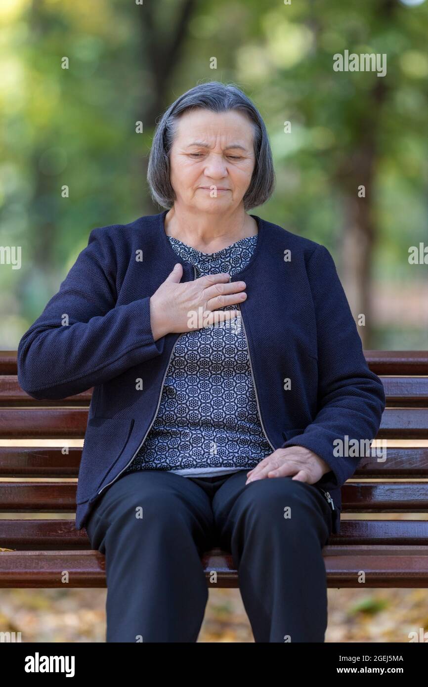 Alternde Frau mit Herzinfarkt. Ältere Dame, die ihre Brust bei den ersten Anzeichen einer Angina oder eines Myokardinfarkts oder eines Herzinfarkts vor Schmerzen festhielt, oben b Stockfoto